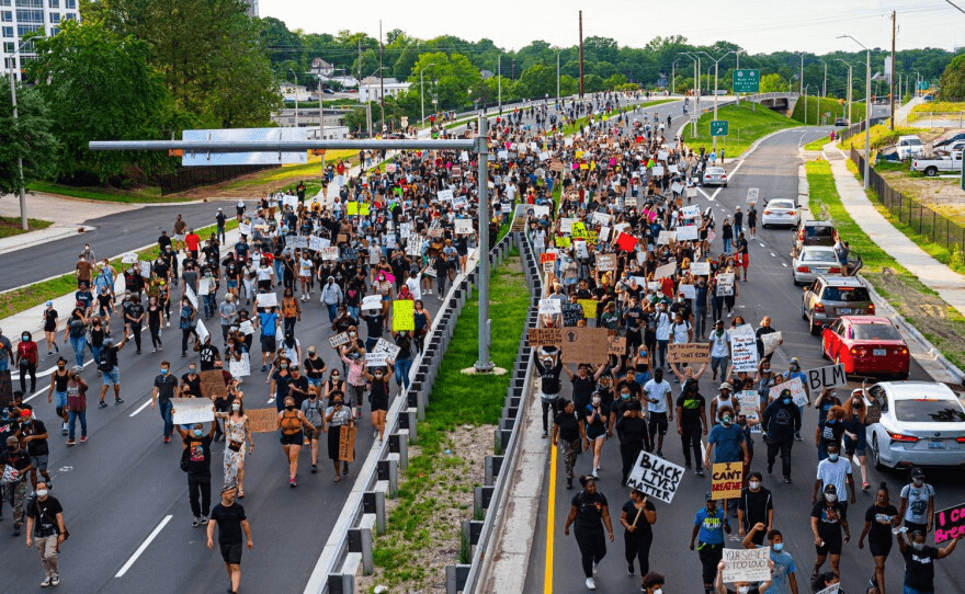 An aerial view of a large crowd marching down a highway in Raleigh, carrying signs.